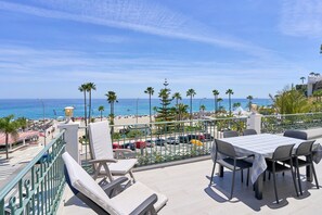 Une terrasse avec une table et des chaises, donnant sur une plage et l’océan.