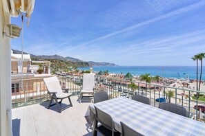 Un balcon avec coin salon extérieur, une table et une vue sur la plage et l’océan.