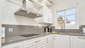 A modern kitchen with white cabinets, a stainless steel range hood, a built-in oven, a sink, and a window with a view of a beach. - Apartment 'Wonderful Penthouse' with Garden, Terrace, Wi-Fi & A/C (Nerja)