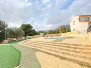 A courtyard with steps leading to a building, a fountain, and a green lawn area.