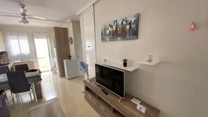 A modern living room with a flat-screen TV, wooden entertainment unit, dining area with chairs, and a kitchen in the background. - Bungalow "Alberca La Nucia" with Mountain view, Terrace & Wi-Fi (polop)