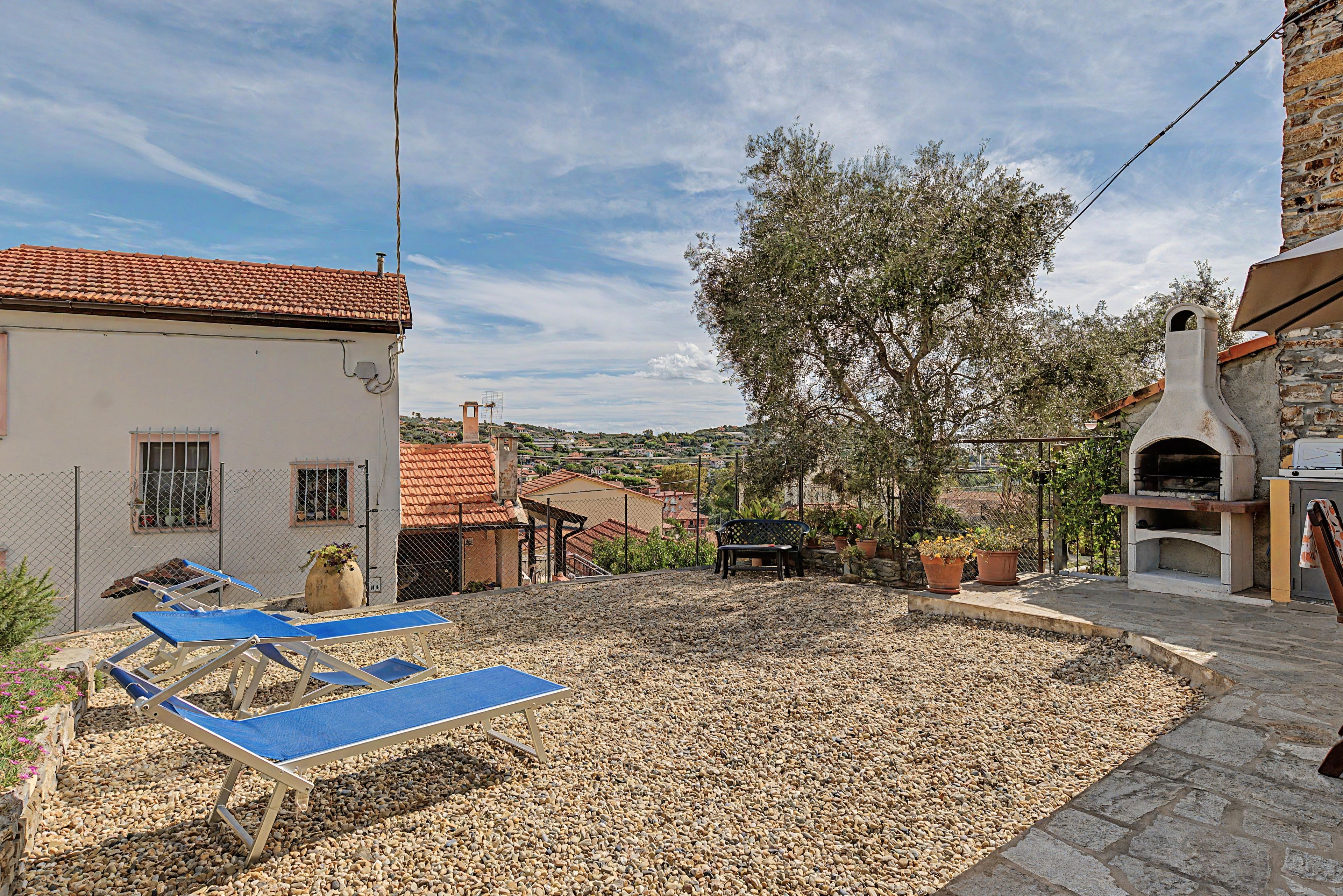 A courtyard with a stone floor, a large tree, and a building with a red-tiled roof.
