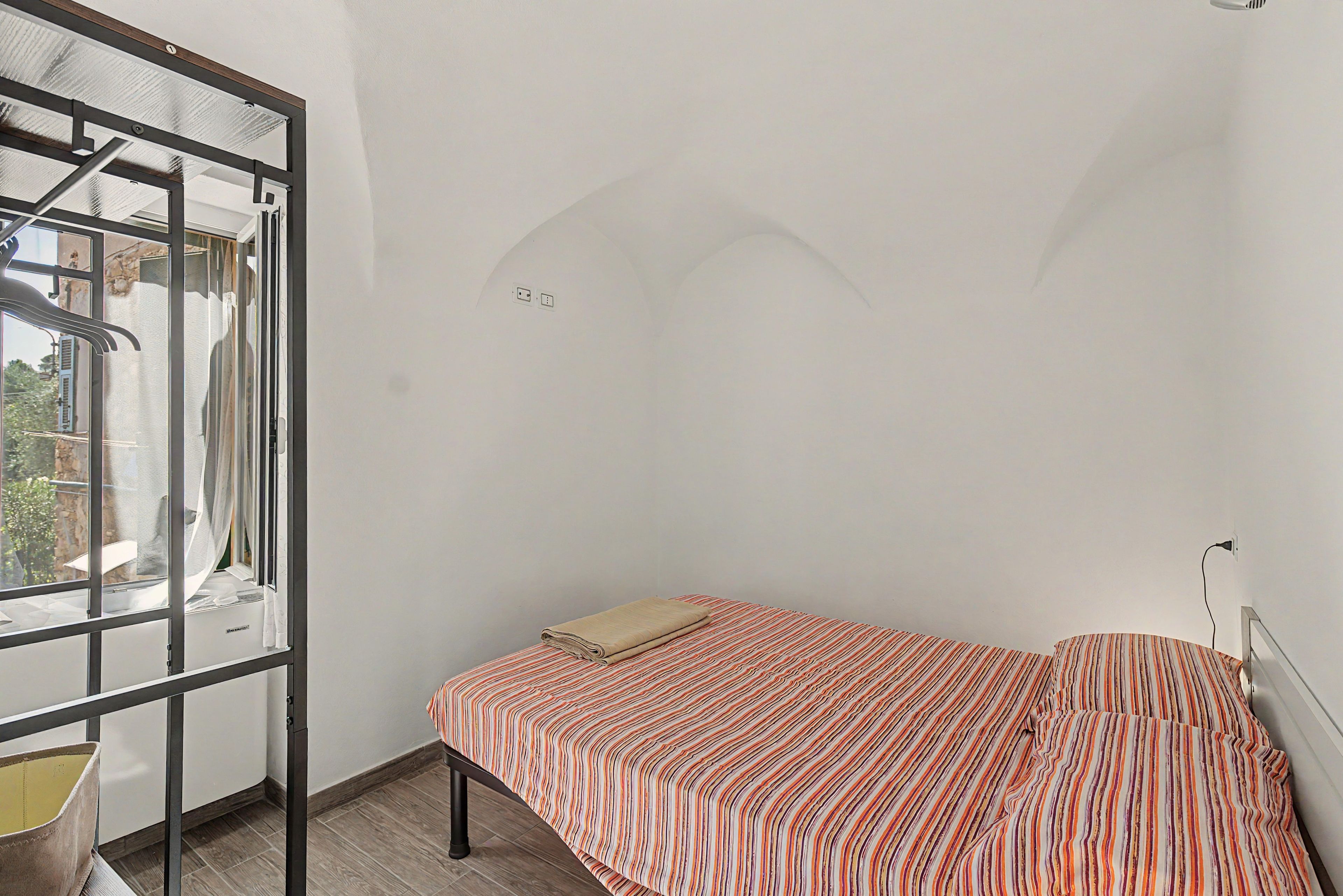 A single bed with a striped bedspread in a room with a window and a door.