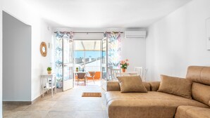 A living room with a sofa, a dining table, chairs, and a view through a glass door to an outdoor area.