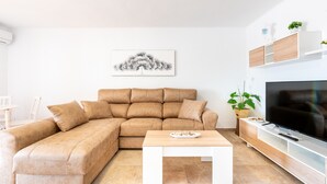 A modern living room with a sectional sofa, a coffee table, a flat-screen TV, and a wall-mounted shelf with plants.