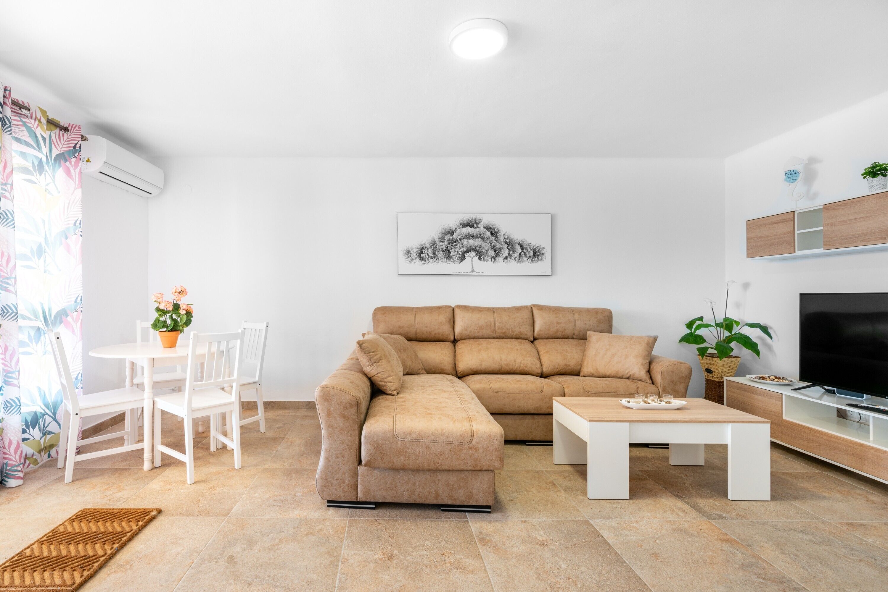 Una sala de estar con un sofá modular, una mesa de centro, un televisor y un comedor con sillas y una mesa.