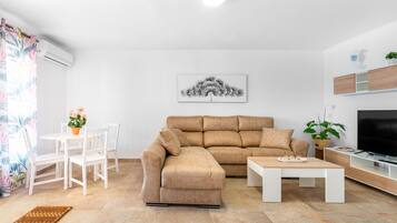 Una sala de estar con un sofá modular, una mesa de centro, un televisor y un comedor con sillas y una mesa.