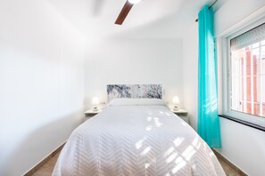 Une chambre à coucher comprenant un lit, deux tables de chevet avec des lampes, une fenêtre avec des rideaux et un ventilateur de plafond.