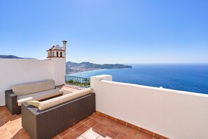 A balcony with a wicker sofa and a small table, overlooking a coastal view with a clear sky. - Holiday home with stunning sea views, private garden, shared pool & Wi-Fi (La Herradura)