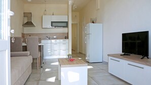 A modern kitchen with white cabinets, a microwave, and a refrigerator. There is a wooden table with a TV on top. - Coastal Escape in Ljubač (Ljubac)