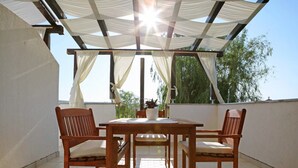 A covered patio with a wooden table and chairs, a potted plant, and a view of trees. - Coastal Escape in Ljubač (Ljubac)