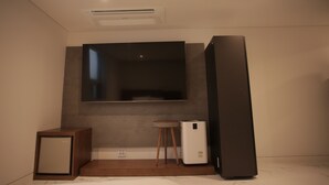 A modern room with a large flat-screen TV mounted on the wall, a small wooden stool, and a white portable heater. - Hotel Seven Step (Siheung)
