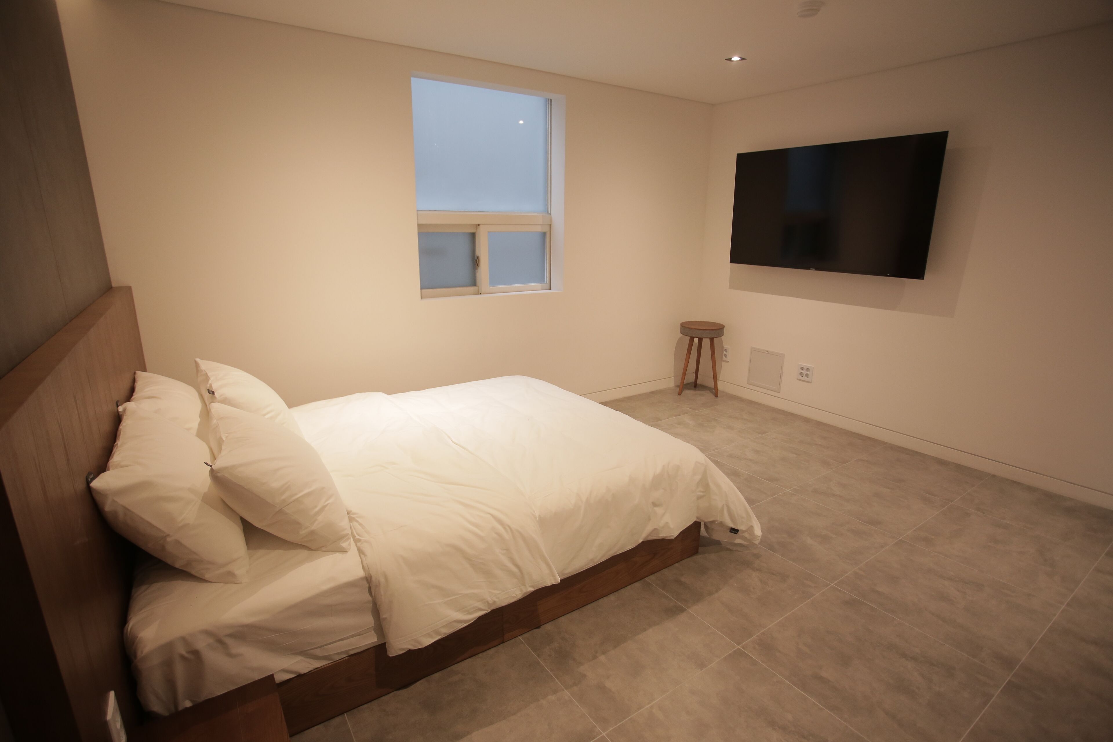 A bedroom with a bed, a window, a television, and a small stool.
