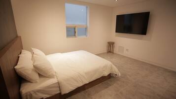 A bedroom with a bed, a window, a television, and a small stool.