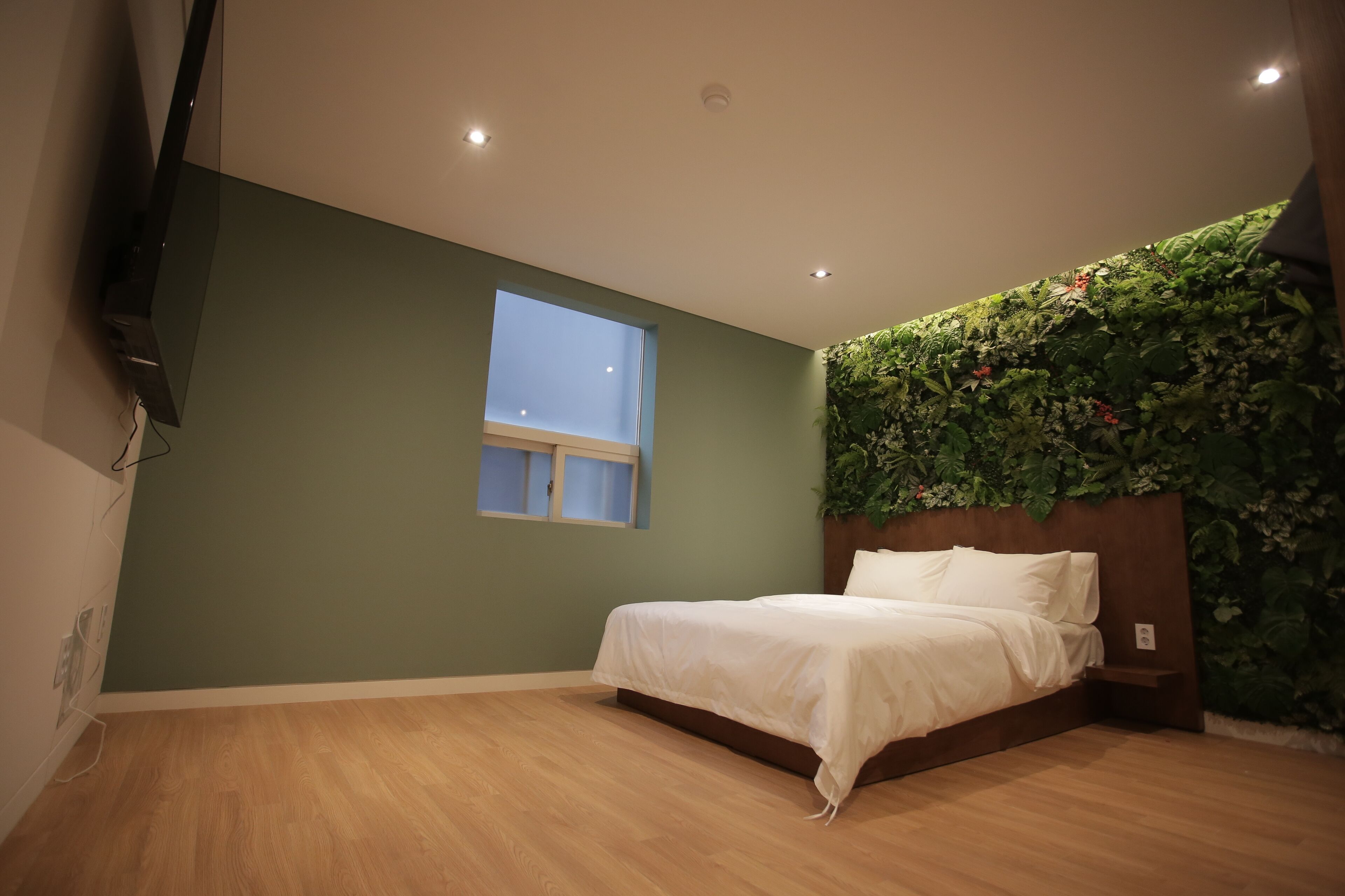 Un dormitorio con una cama, una ventana y una pared con un diseño de hojas verdes.