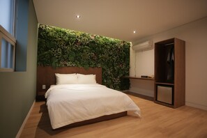 A bedroom with a bed, a wooden headboard, a wall-mounted plant, a wooden wardrobe, and a small desk with a mirror. - Hotel Seven Step (Siheung)