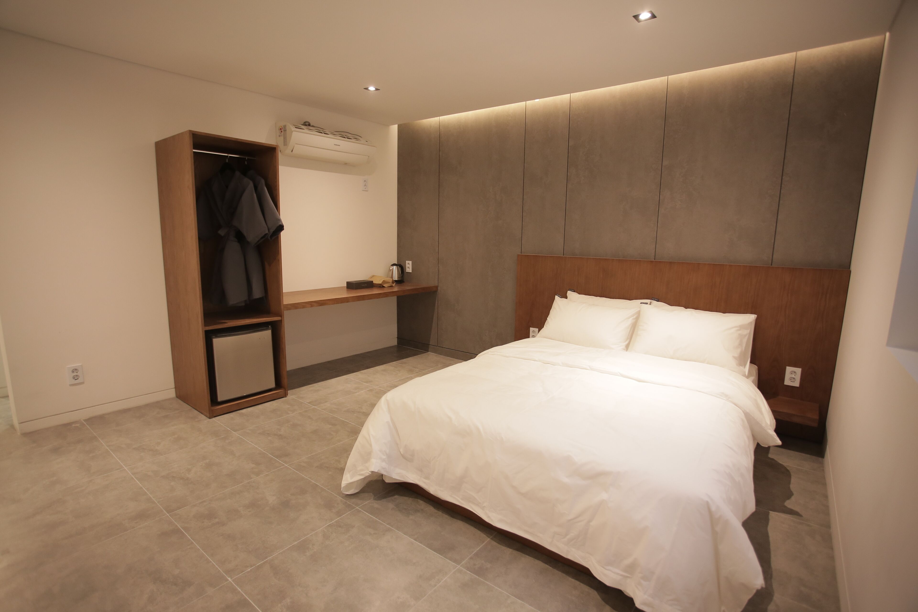 A modern bedroom with a large bed, a wooden wardrobe, and a small bedside table.