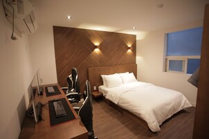 Una habitación de hotel moderna con cabecera de madera, una cama individual, un escritorio con una computadora y una silla.