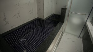 A bathroom with a glass shower enclosure, a black tiled floor, and white marble walls. - Hotel Seven Step (Siheung)