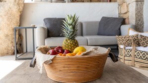 A wicker fruit basket with a pineapple, apples, and oranges on a table in a living room with a stone wall and a grey sofa. - Luxe Côte Stay- Elegant Villa (Porto Cervo)