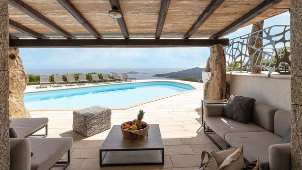 A poolside area with a wooden pergola, lounge chairs, a sofa, and a table with fruit. - Luxe Côte Stay- Elegant Villa (Porto Cervo)
