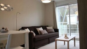 A modern living room with a dark brown sofa, a white coffee table, and a dining area with a white table. - 57 M2 FLAT WITH SEA AND BEACH VIEWS (Le Portel)