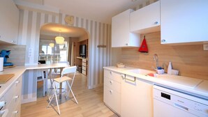 A modern kitchen with white cabinetry, a dining area with a table and chairs, and a built-in dishwasher. - 57 M2 FLAT WITH SEA AND BEACH VIEWS (Le Portel)