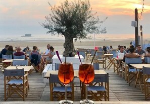 An outdoor dining area with tables and chairs, a large tree, and a view of the sea. - 57 M2 FLAT WITH SEA AND BEACH VIEWS (Le Portel)