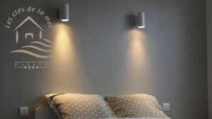 A bedroom with a bed, two wall-mounted lights, and a wall decal with a house and waves. - 57 M2 FLAT WITH SEA AND BEACH VIEWS (Le Portel)