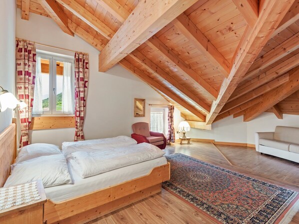 Un dormitorio con techo de madera, una cama, una silla, un sofá y una alfombra.