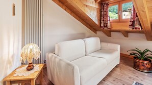 Una habitación acogedora con techo de madera, un sofá blanco, una mesa con lámpara y una ventana con cortinas.