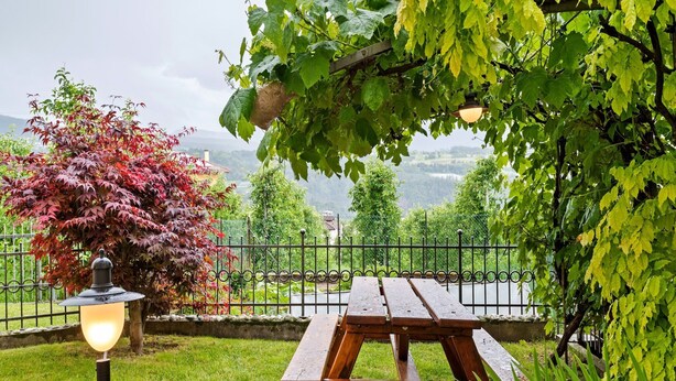 A wooden picnic table, a lamp post, and a view of a green landscape with trees and a fence.