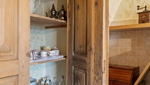 A wooden pantry with shelves holding kitchenware, a spice rack, and a wooden chest.