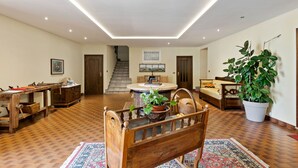 A spacious living room with a wooden floor, a round coffee table, a sofa, and a dining table with chairs. There is a staircase in the background leading to another level.