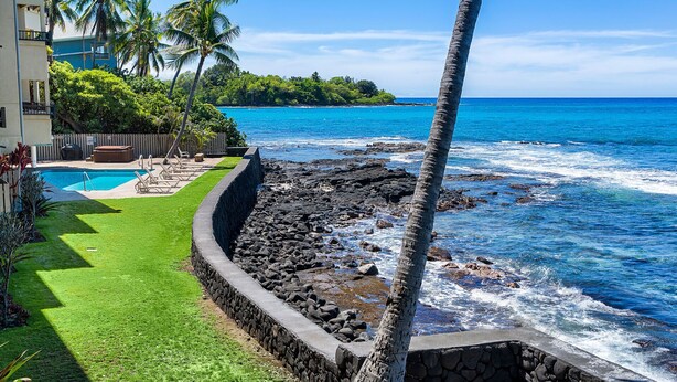 A coastal property with a swimming pool, a stone retaining wall, and a view of the ocean. - Oceanfront Banyan Tree 200 in Kailua Kona, 2BR, 2BA, perfect for 4 guests. (Kailua Kona)