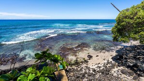 A beach with clear water, rocks, and greenery. - Oceanfront Banyan Tree 200 in Kailua Kona, 2BR, 2BA, perfect for 4 guests. (Kailua Kona)