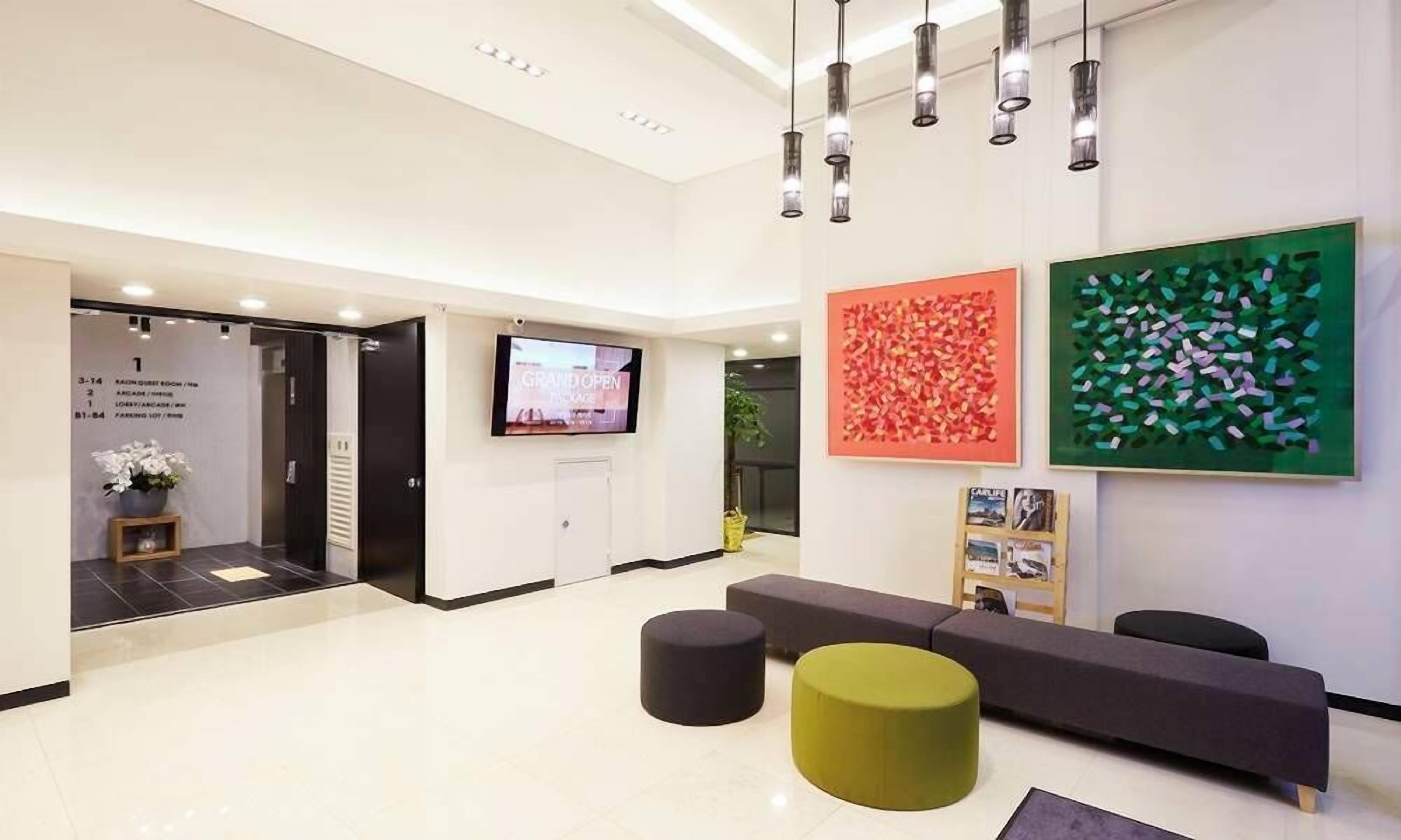 A modern reception area with a flat-screen TV, a large green and red abstract art piece, and a seating area with a grey sofa and two stools.