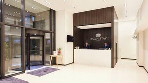 Ein Hotel-Empfangsbereich mit modernem Design, der einen Empfschalter, einen digitalen Bildschirm und einen Glastürdurchgang zeigt.