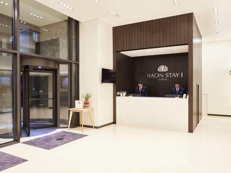 Een receptiegebied van een hotel met een modern ontwerp, met een receptiebalie, een digitaal scherm en een glazen ingang.
