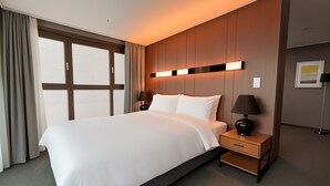 Ein Hotelzimmer mit einem großen Bett, einem Nachttisch, einer Lampe und einem Fenster mit Vorhängen.