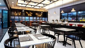 Ein modernes Restaurant mit mehreren Tischen und Stühlen, einem Küchenbereich mit Edelstahlgeräten und großen Fenstern, die einen Blick auf die Stadt bieten.