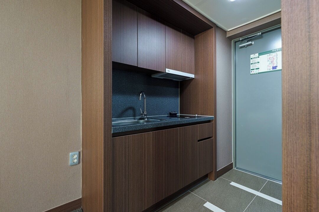 Una cocina compacta con armarios de madera oscura, un lavamanos de acero inoxidable y una campana extractora blanca.