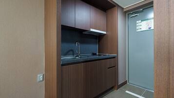 Una cocina compacta con armarios de madera oscura, un lavamanos de acero inoxidable y una campana extractora blanca.