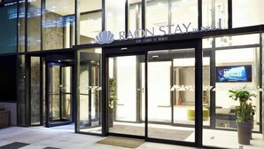Das äußere Erscheinungsbild eines Hotels namens RAONSTAY in Perla, mit Glastüren und einem sichtbaren Innenzeichen.