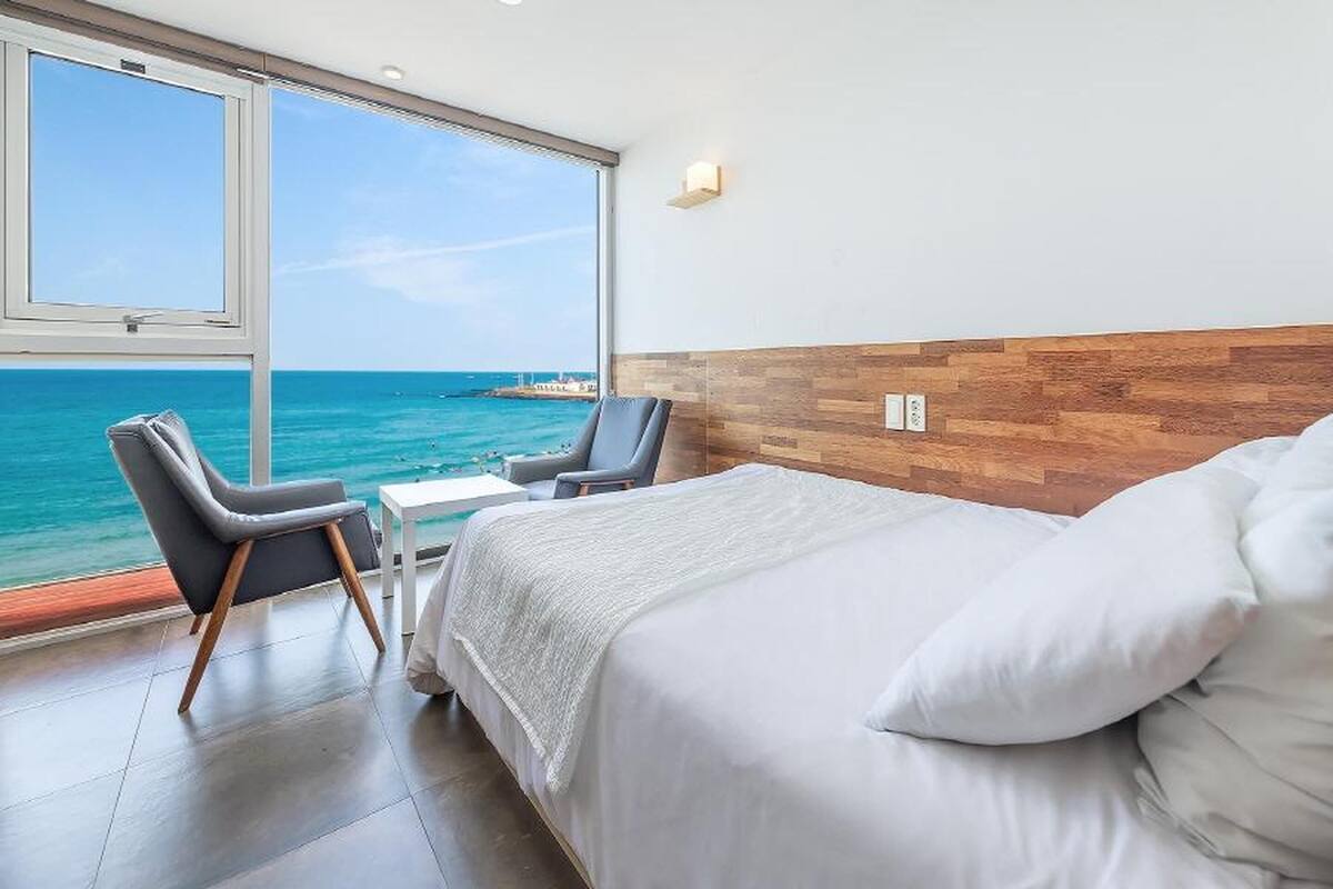 A bedroom with a large window, a bed, two chairs, and a small table.