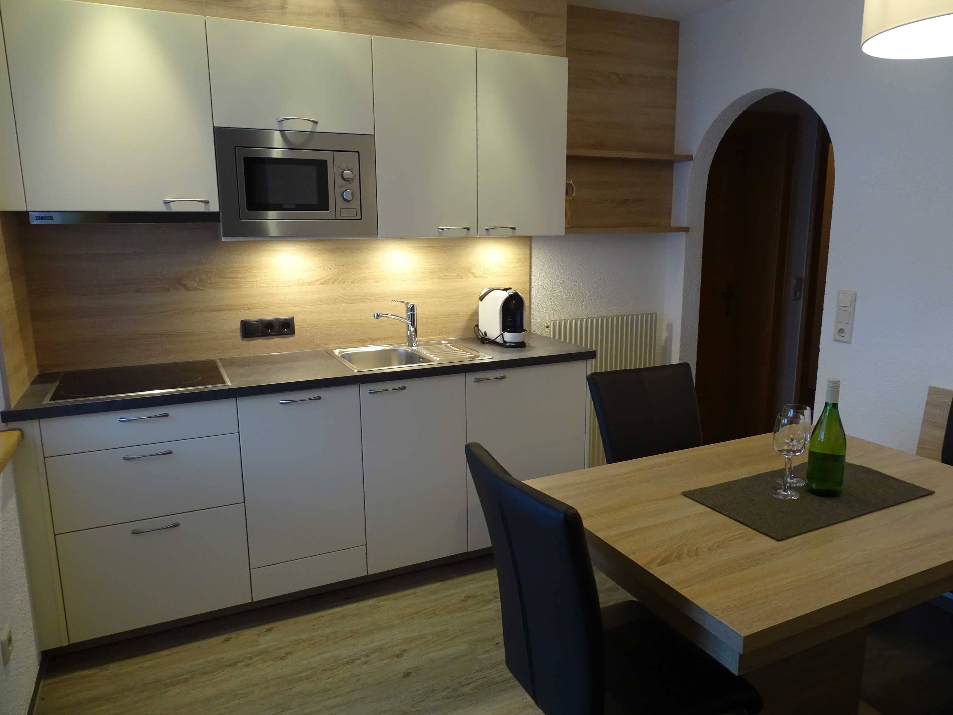 Een moderne keuken met een magnetron, spoelbak en een eethoek met een tafel en stoelen.
