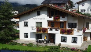 A two-story building with balconies, a patio area, and a mountain backdrop. - Stables - Alpenfrieden (Nauders)