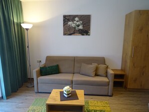 En stue med sofa, sofabord med blomsterarrangement, lampe og et maleri på væggen.