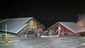 Ein rustikaler Holenstall mit Metallbedachung, umgeben von einem Holzzaun und schneebedecktem Boden.
