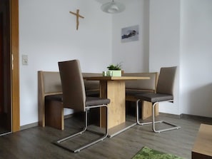 Une pièce avec une table en bois et deux chaises, une croix accrochée au mur et une petite plante posée sur la table.